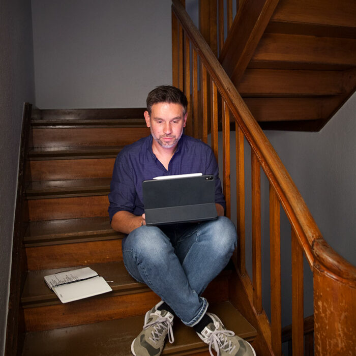 Benjamin Wockenfuß sitzt auf Treppe mit iPad und Notizbuch